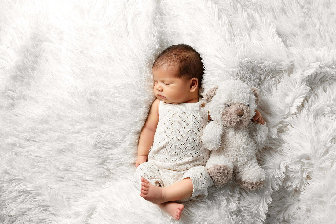 Un bébé dormant paisiblement avec son doudou bébé doux sur un doux plaid blanc.