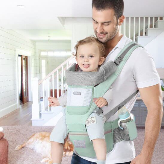 Porte bébé comfort + utilisé par un parent à la maison, montrant un enfant souriant et un design ergonomique.